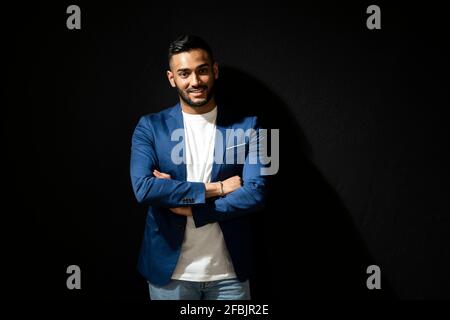 Confident man with arms crossed standing against black background Stock Photo