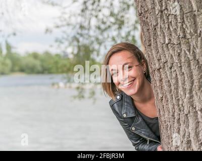 Portrait of laughing woman hiding behind tree trunk Stock Photo