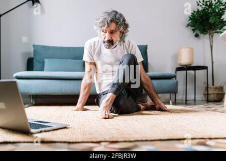 Man doing yoga on carpet while watching tutorial on laptop at home Stock Photo