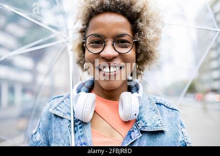 Happy woman wearing wireless headphones holding umbrella Stock Photo