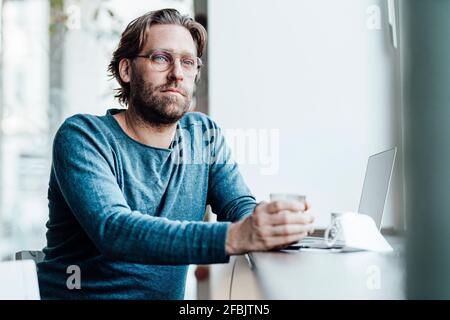 Thoughtful man by laptop in coffee shop during pandemic Stock Photo