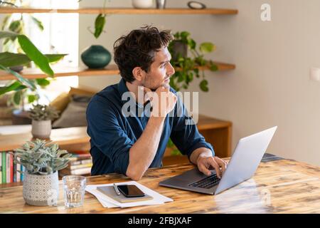 Male freelance worker contemplating while using laptop at table Stock Photo