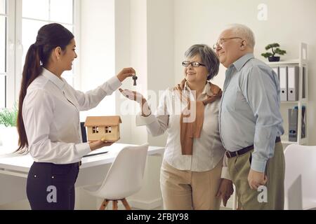 Female real estate agent give key from new home to excited elderly client couple Stock Photo