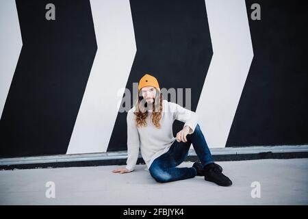 Relaxed man sitting on footpath in front of wall Stock Photo