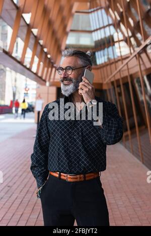 Smiling mature bearded man talking on mobile phone on walkway Stock Photo