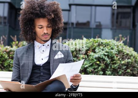 Young male entrepreneur examining documents in file while sitting on bench Stock Photo