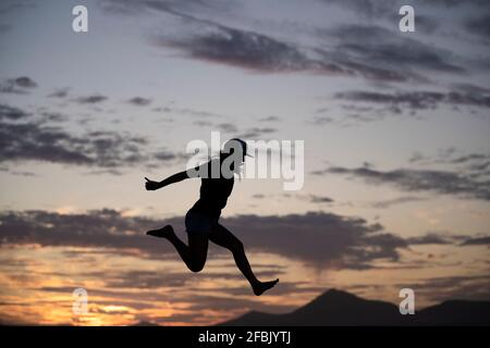 Excited woman jumping during sunset Stock Photo