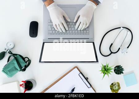 Male doctor wearing surgical glove typing on laptop Stock Photo