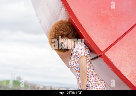 Redhead young woman standing by red curve wall Stock Photo