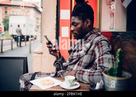 Fashionable young man using mobile phone at sidewalk cafe Stock Photo