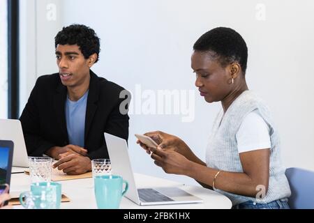 Businesswoman using mobile phone while sitting with colleague at office Stock Photo
