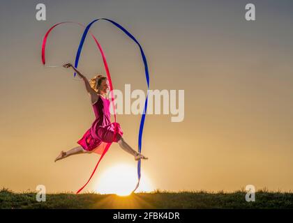 Woman with ribbons doing gymnastics during sunset Stock Photo