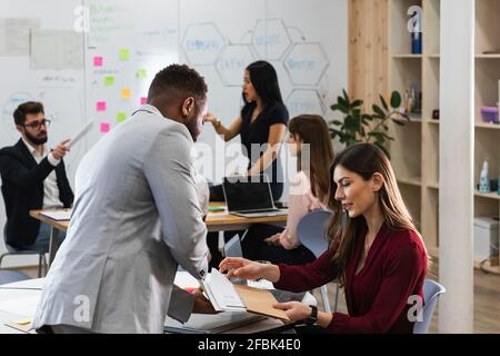 Male and female entrepreneurs discussing over documents with colleagues in background at office Stock Photo