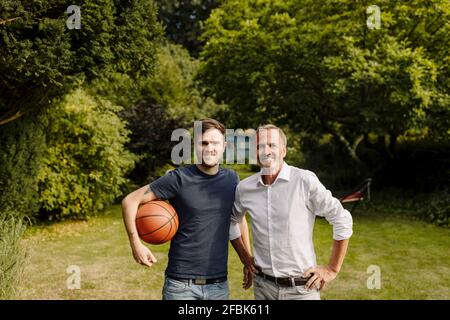 Son holding basketball while standing by father in backyard Stock Photo