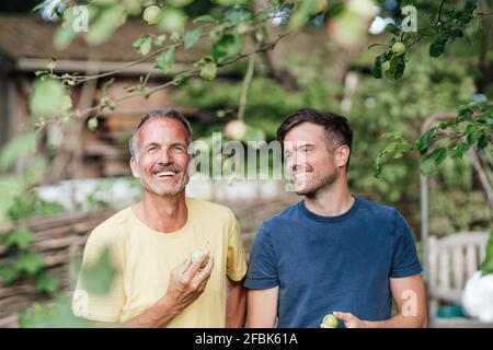 Father and son holding Granny smith apple while standing in backyard Stock Photo