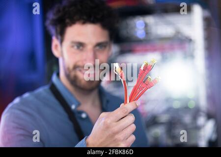Smiling male IT professional with patch cord cable standing in data center Stock Photo