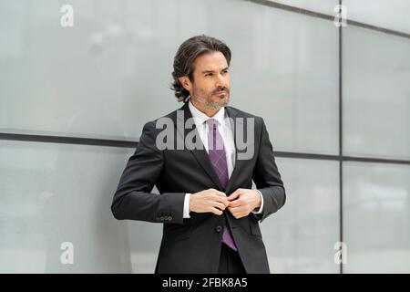 Serious businessman looking away while wearing suit against wall Stock Photo