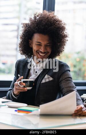 Happy young male entrepreneur analyzing document while having coffee in cafe Stock Photo
