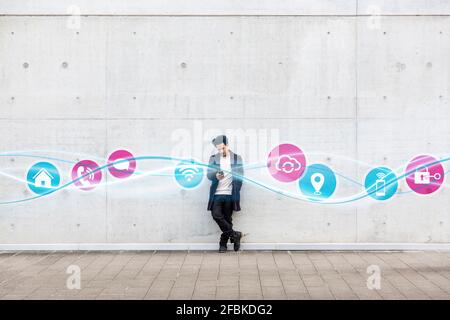 Young man using mobile phone while standing with icons on glowing wave pattern on footpath Stock Photo