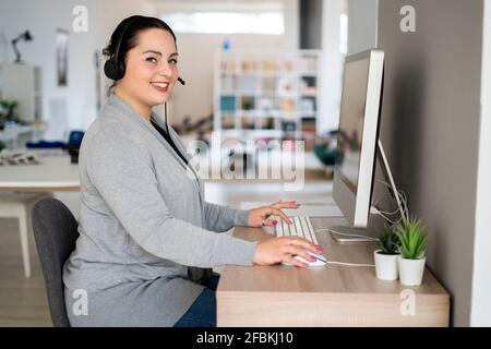 Smiling female customer service representative using computer while working at home office Stock Photo