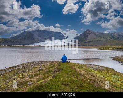 Mid adult man looking at view while sitting in front of lagoon, Breidamerkurjokull Glacier Stock Photo