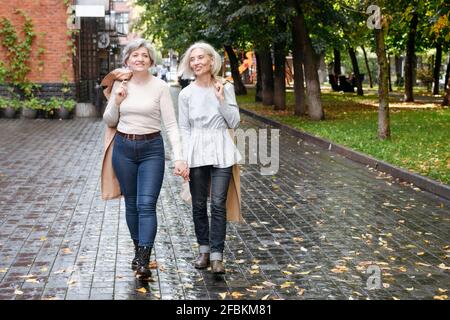 Smiling female friends walking on wet footpath during autumn Stock Photo