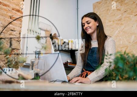 Smiling beautiful female owner using laptop in florist's shop Stock Photo
