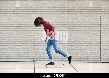 Curly haired man skateboarding by wall Stock Photo