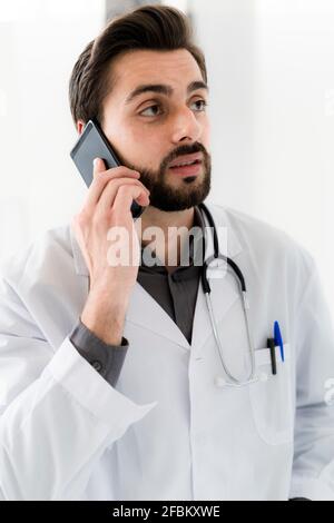 Handsome male healthcare worker talking on smart phone while looking away Stock Photo