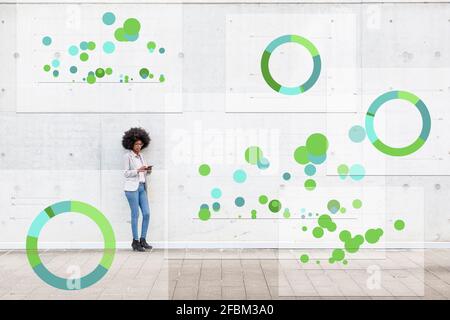 Businesswoman using mobile phone while standing with pie chart icons around on footpath Stock Photo