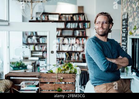 Smiling male owner with arms crossed sitting in cafe Stock Photo