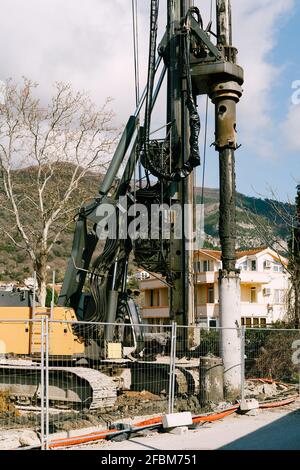 Crawler tractor with a drilling rig works behind a fence against the backdrop of a house Stock Photo