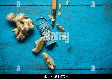 Ginger root, grater and kitchen knife lying on blue wooden surface Stock Photo