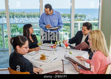 Miami Florida,Coconut Grove Sonesta hotel Panorama restaurant,Biscayne Bay view dining table,waiter taking writing order diners ordering women man, Stock Photo