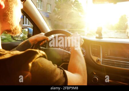 Young man in black t-shirt holding steering wheel, driving car, forearm tattoo, hands close up. Dashboard panel, phone holder mount. Male inside vehic Stock Photo