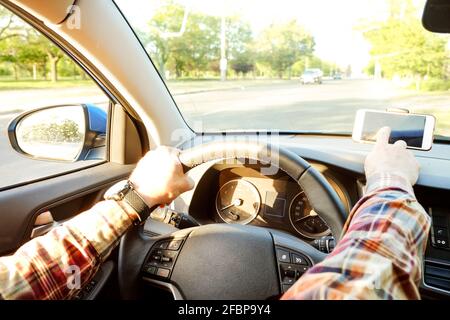 Young man hand on steering wheel driving car touching smartphone w/ black screen. Dashboard panel, phone holder mount. Male hipster drives automobile, Stock Photo