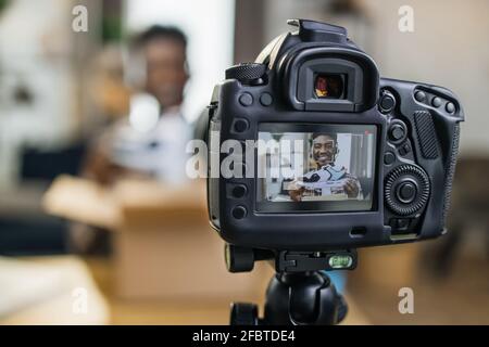 Afro american man unboxing brand new sneakers at home and recording video on professional camera. Young blogger creating online content for his channel. Stock Photo