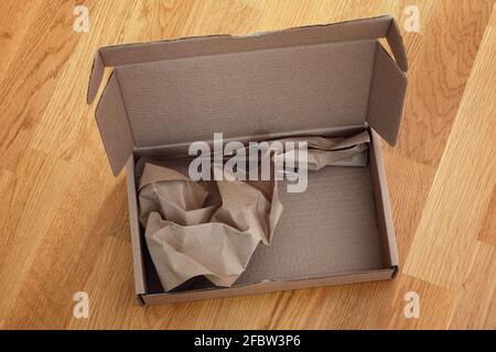 Open cardboard box with crumpled paper inside on a wooden background. Close up. Stock Photo