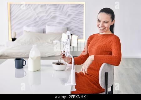 An adult woman uses phone holder at dining table. Stock Photo