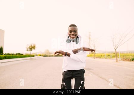 Young african American black man with afro hair dancing in the middle of the street wearing a white sweatshirt, black pants and wireless headphones. H Stock Photo