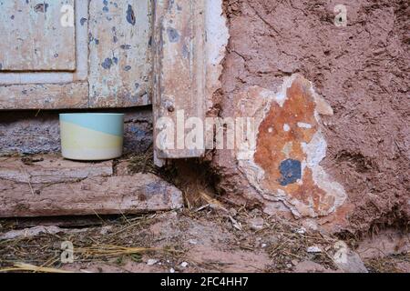 Selective focus on colorful plaster pot for cactuses in front of an old, rustic, wooden door of a house made from mud and some hay on the ground Stock Photo