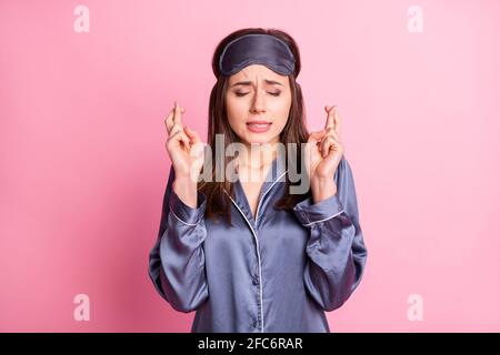 Photo portrait of hopeful girl with closed eyes fingers crossed isolated on pastel pink colored background Stock Photo