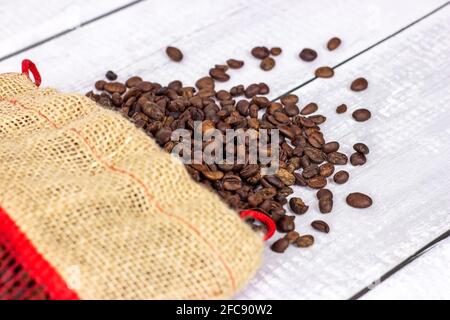 Fresh roasted brown organic arabica coffee beans in a burlap bag on light wooden background. Stock Photo