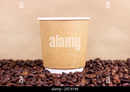 Brown cardboard disposable cup with coffee and roasted coffee beans on the table with copy space on light background. Takeaway food concept. Stock Photo