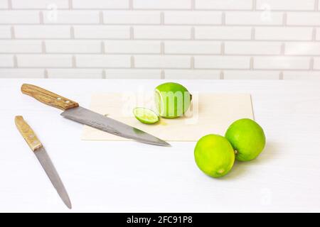 Fresh green sour lime cut with the knife on light wooden cutting board in the kitchen. Stock Photo