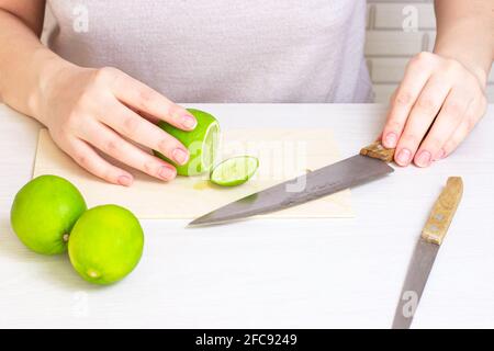 Fresh green sour lime cut with the knife on light wooden cutting board by woman hands in the kitchen. Stock Photo
