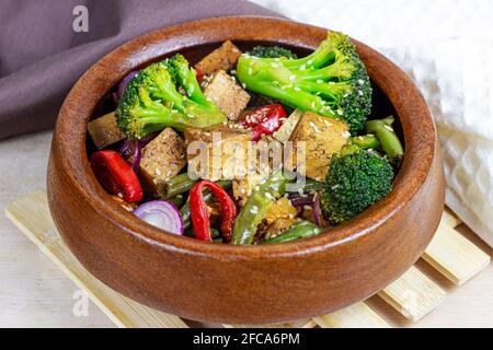 Homemade vegetarian fried tofu with vegetables (broccoli, pepper, onions and green beans) in the wooden bowl. Stock Photo