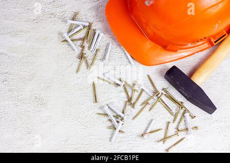 Top view of orange protective hard hat with claw hammer on light gray cement with copy space. Home repairing and improvement, house building concept. Stock Photo