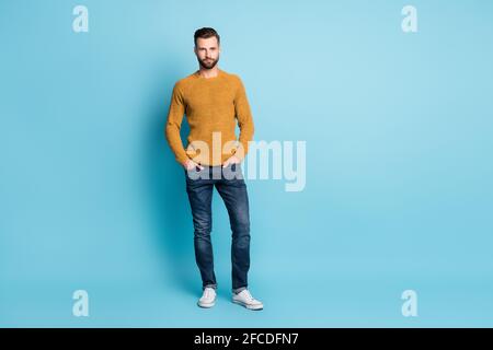 Full size photo of young handsome serious man hold hands in pockets wear knitted sweater isolated on blue color background Stock Photo