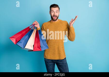 Portrait of attractive amazed cheerful guy holding in hands pile bags things having fun isolated over bright blue color background Stock Photo
